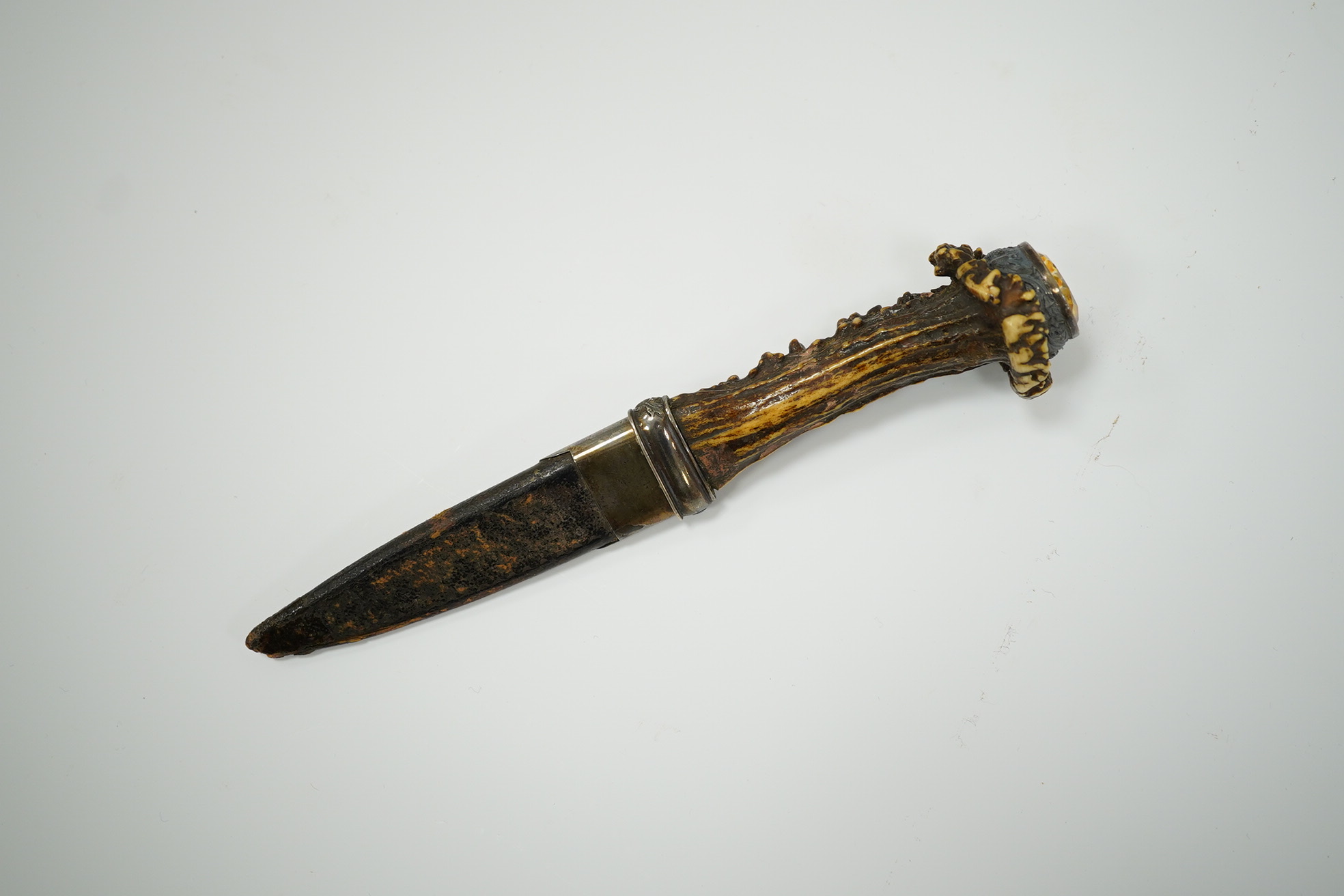 A late 19th century Scottish traditional sgian dubh with foiled glass mounted deer antler handle, and silver coloured metal mounts with thistles in relief, blade 10cm. Condition - fair, missing chape.